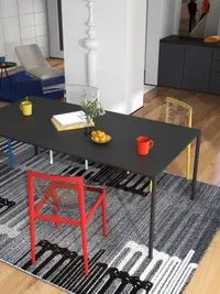 Black dining table with red and yellow chairs on a patterned grey rug in sunlight