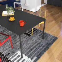 Black dining table with red mug books and clear chairs on a grey patterned rug