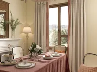 Dining room with pink tablecloth flowers plates window view of forest fireplace and ceiling light
