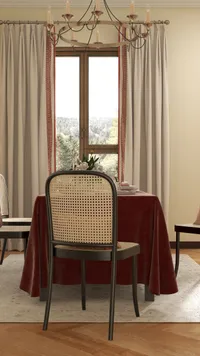 Dining room with red table cloth, woven chair, ceiling light, window curtains, and forest view