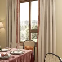 Elegant dining table setting with pink tablecloth, glass tableware, cane chairs, and light beige curtains
