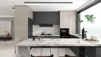 Modern kitchen with grey cabinets, wood cabinets, marble counter, stove, sink, and green indoor plant