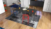 Open interior showing black dining table, colorful plastic chairs, patterned rug, kitchen, and blue carpet