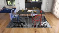 Modern black dining table with colorful chairs on patterned rug in an open plan area