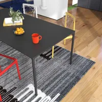 Close up of black dining table with orange mug, fruit bowl, books, and red chair