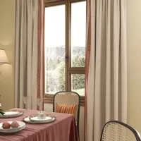Close up of dining table with pink tablecloth plates glass window curtains and woven chair