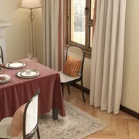 Dining table with red cloth, chairs with pillows, plates, glasses, rug, and window with curtains