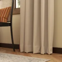 Close up of beige curtains next to a chair on wood floor and patterned rug