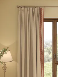 Light beige curtain with orange border pattern hanging next to wooden window and table lamp
