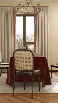 Dining table with red tablecloth wooden chairs woven backs beige curtains and a ceiling light