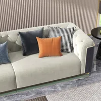 Beige sofa with orange and grey pillows on marble floor next to a ribbed wall panel