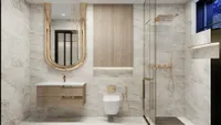 Modern marble bathroom featuring a wooden cabinet gold mirror white toilet and glass shower door