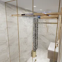 Modern bathroom shower with water falling from wooden ceiling fixture, marble walls, and gold frame