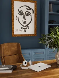 Modern home office desk with white laptop, headphones, brown leather chair, and blue storage drawers